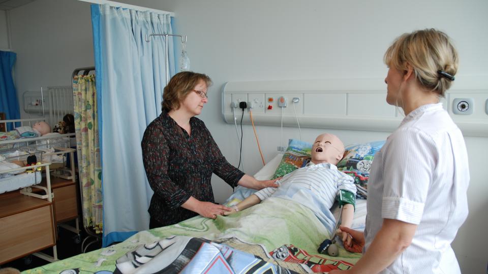 Two women in a nursing simulation room with a dummy patient
