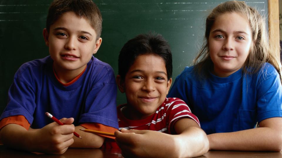 Three children leaning on a desk smiling