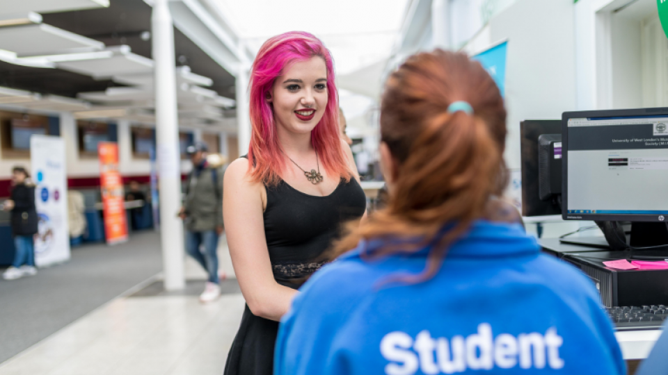 A student ambassador liaising with a student at a help desk on campus.