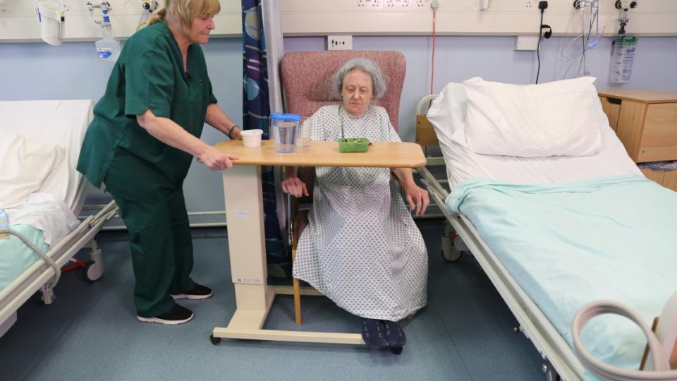 Patient sitting in a chair on a ward speaking to a nurse