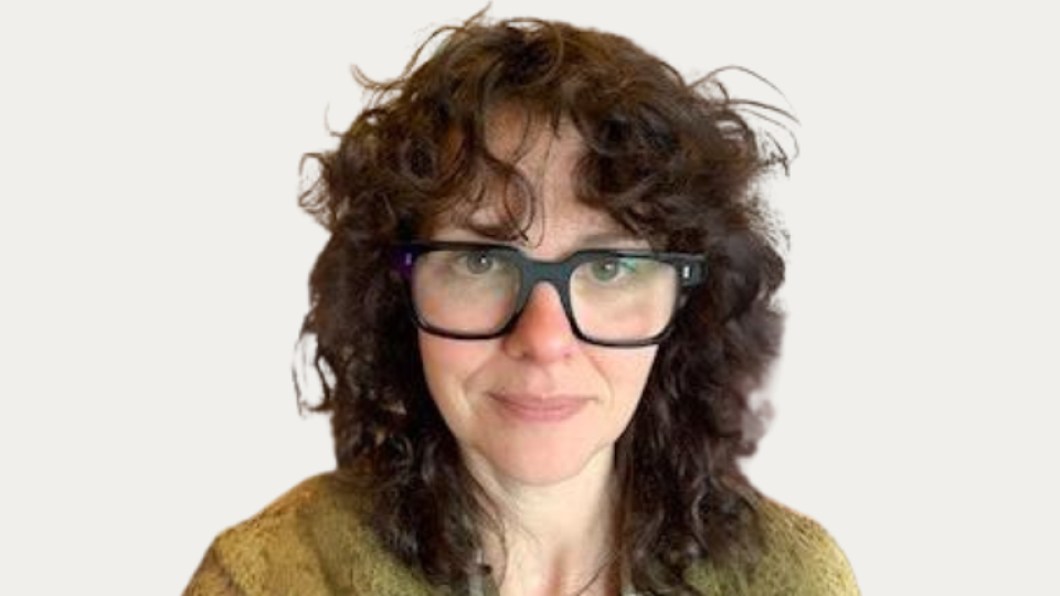 Danielle Woods is wearing glasses and has shoulder-length brown curly hair.