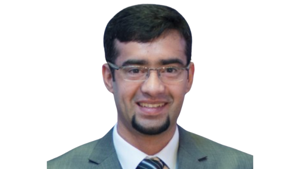 Dr Waqar Asif is wearing a grey suit and tie and has short dark hair and glasses.