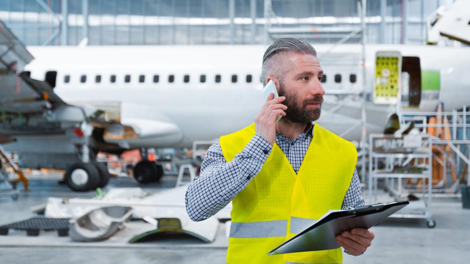 A man on a mobile phone wearing a high-vis vest in front of an airplane