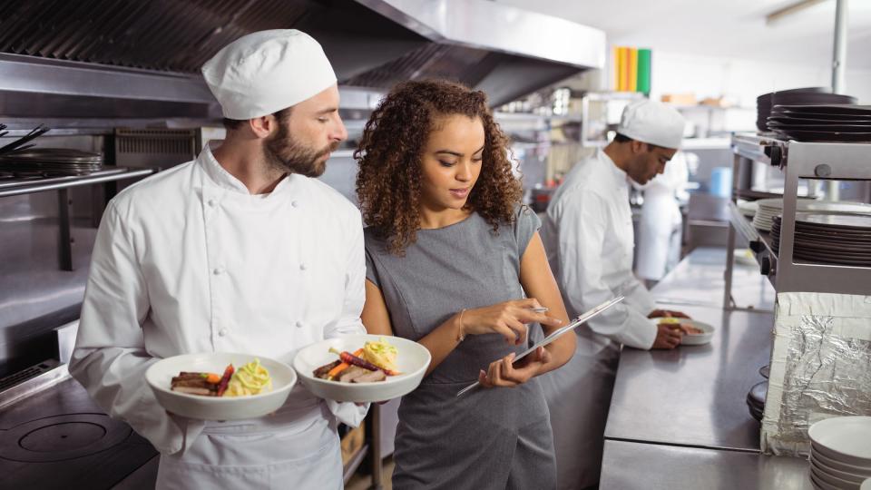 A female in grey business dress showing something on her tablet to a chef holding food