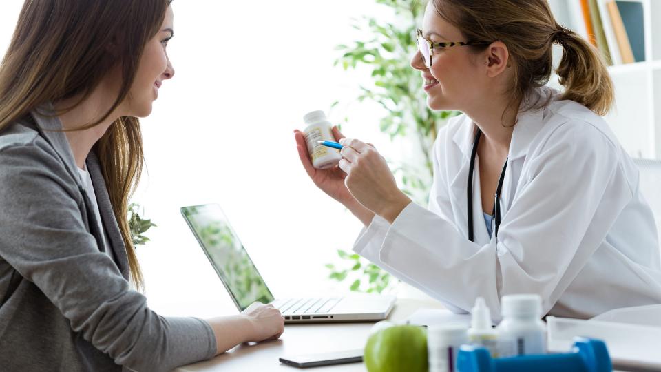 A female doctor wearing glasses giving pills to a female patient in an office