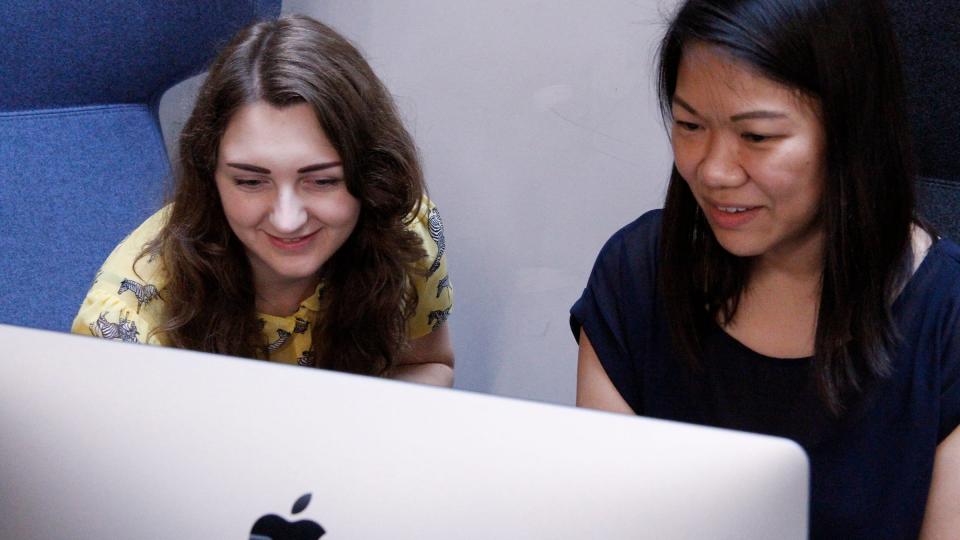 Two female students looking at a Mac monitor