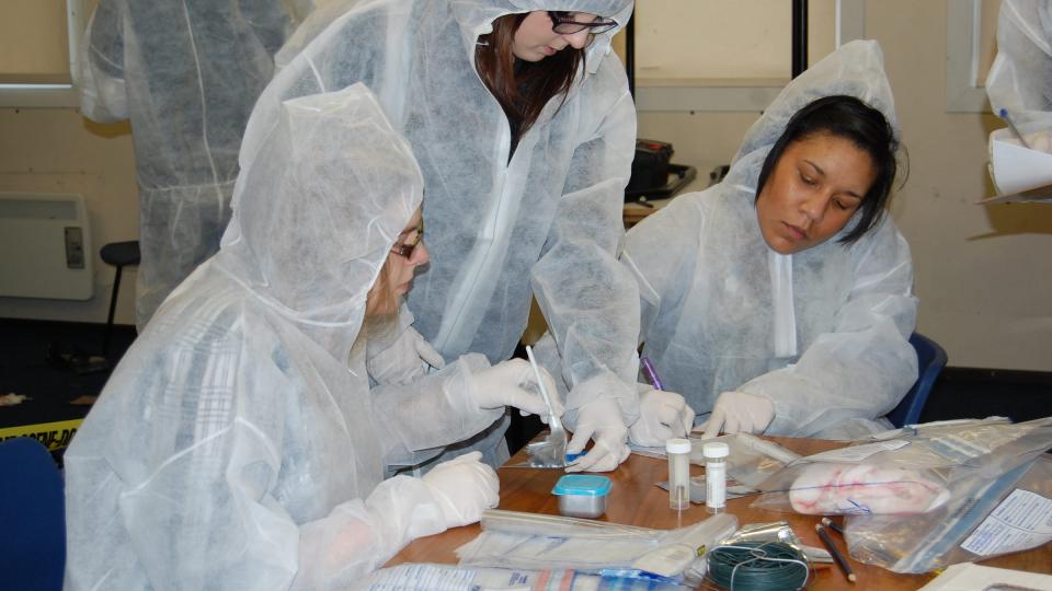 Students in white forensic body suits carrying out experiments