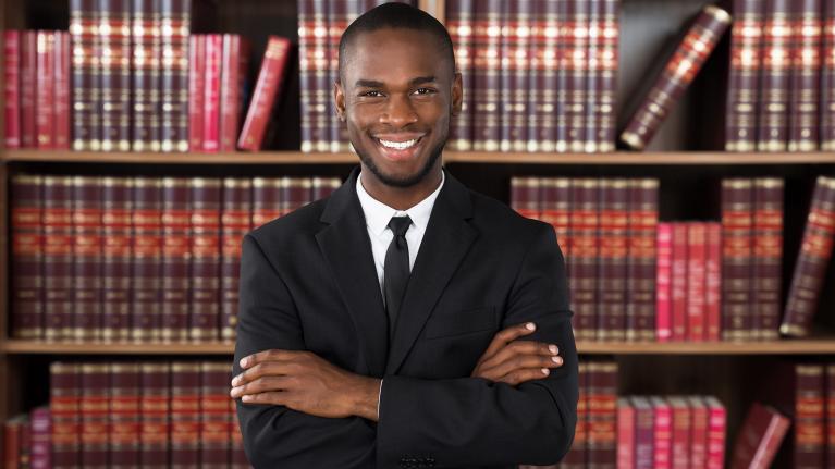 A smiling man in a suit standing in front of a shelf of legal books