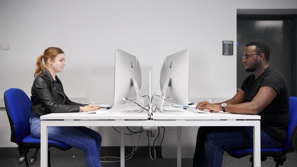 Woman and man working on desktop Macs facing each other