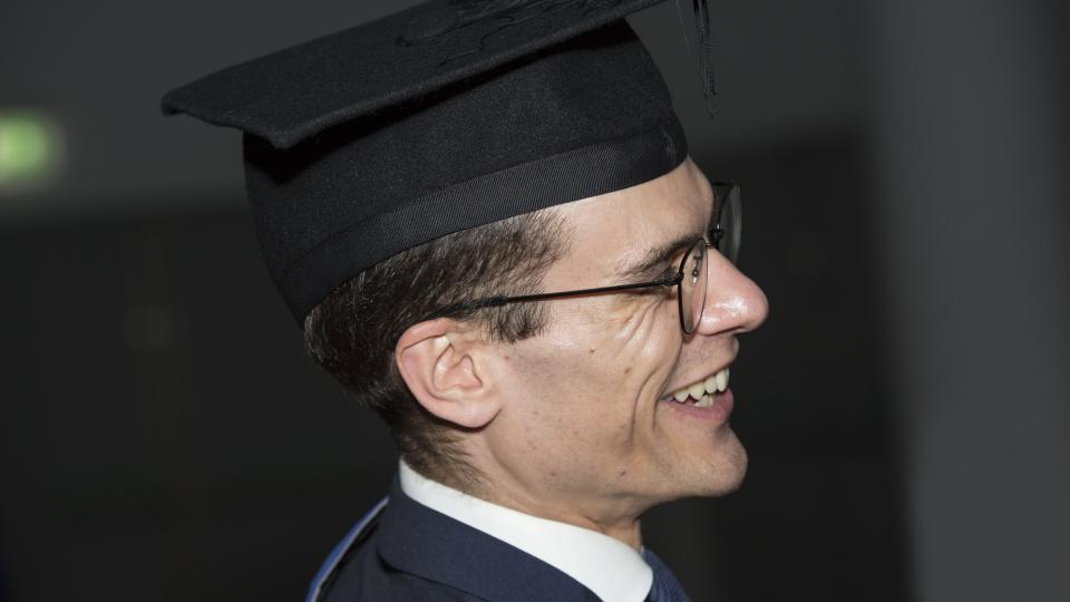 Man in a graduation cap and glasses smiling
