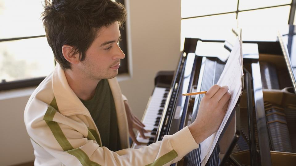 A student at a piano, writing on manuscript paper