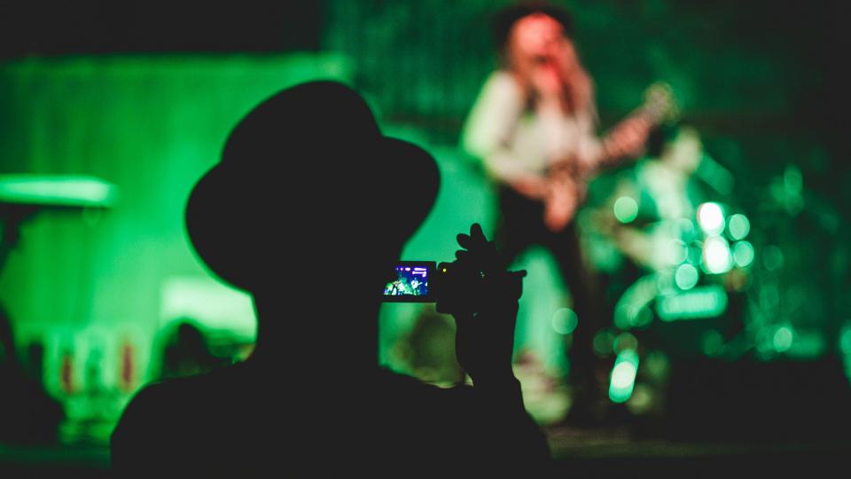 live guitarist playing at a concert with an audience member making a smartphone recording.