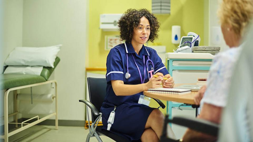 A&E nurse in a blue uniform talking to a patient in a consulting room 