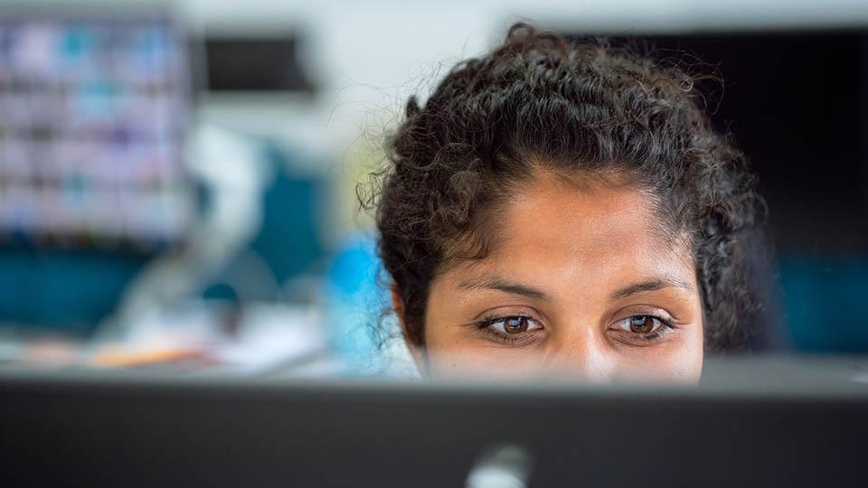 medium close-up of an engineer with dark curly hair working at a computer