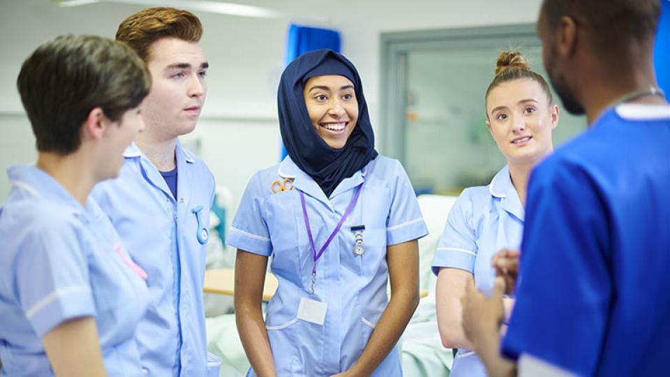 A mixed group of nursing students on the ward dressed in blue uniforms 