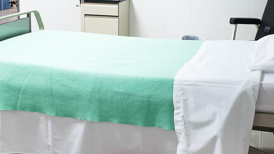 an empty hospital bed with a green blanket on it