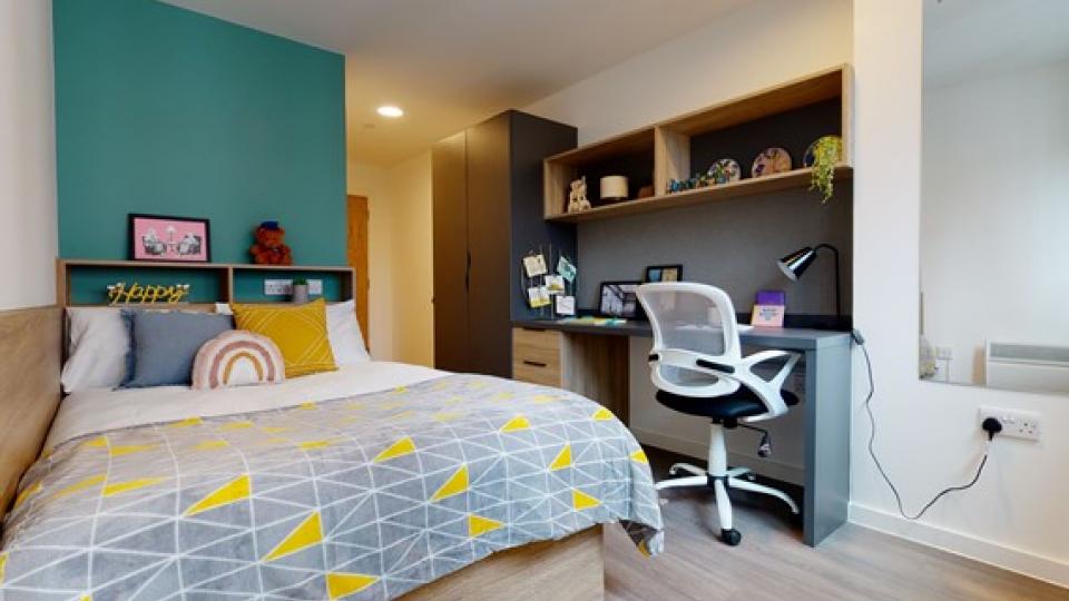 a student accommodation bedroom located in Canvas Wembley with bright blue walls a single bed and a working space with the chair and desktop