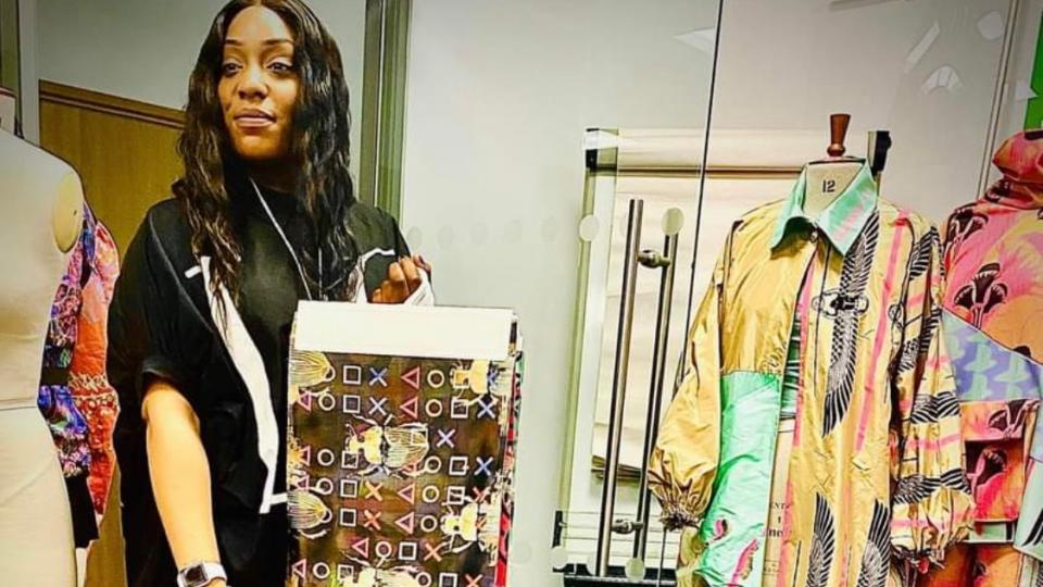 Fashion student Chevon Blanc holding a bag and surrounded by colourful clothes she designed