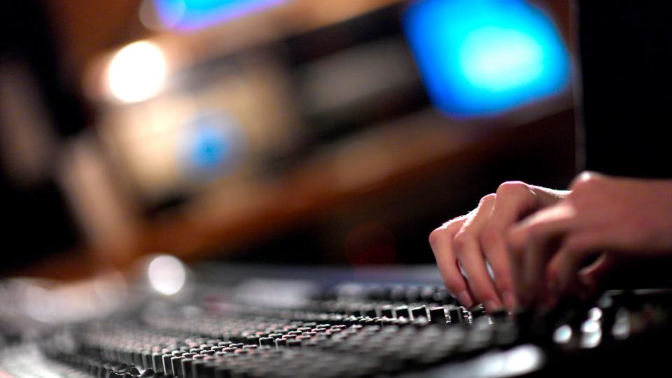 A pair of hands turning dials on a mixing desk in a music studio