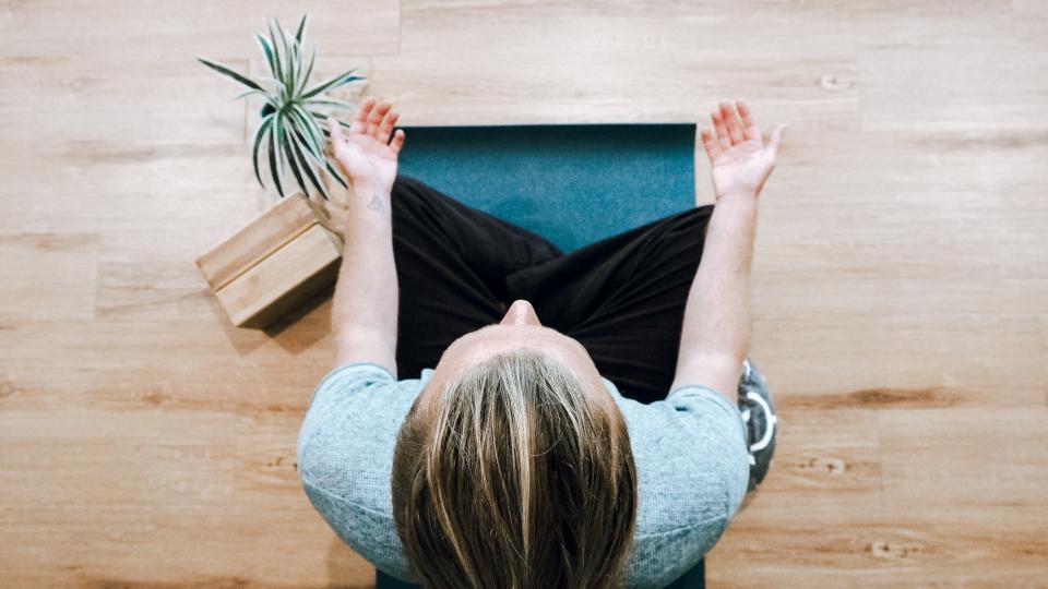 A lady meditating on a mat with her palms facing upwards on her legs.