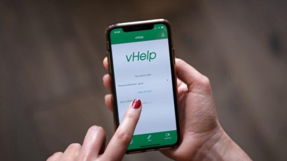 person touching phone with vHelp app showing on screen.