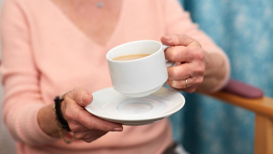 A lady holding a cup of tea and saucer.