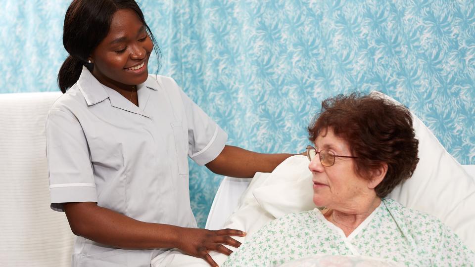 A care worker helping a patient in a care home bed.