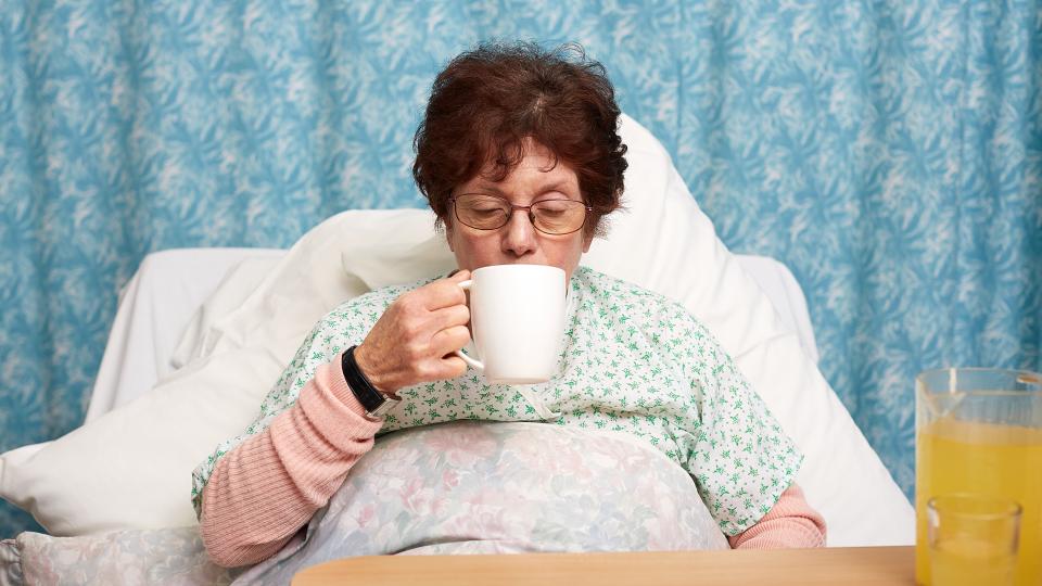 A patient drinking a hot drink in a care home bed.
