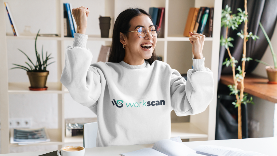 A female wearing a Workscan hoodie celebrating at her desk.