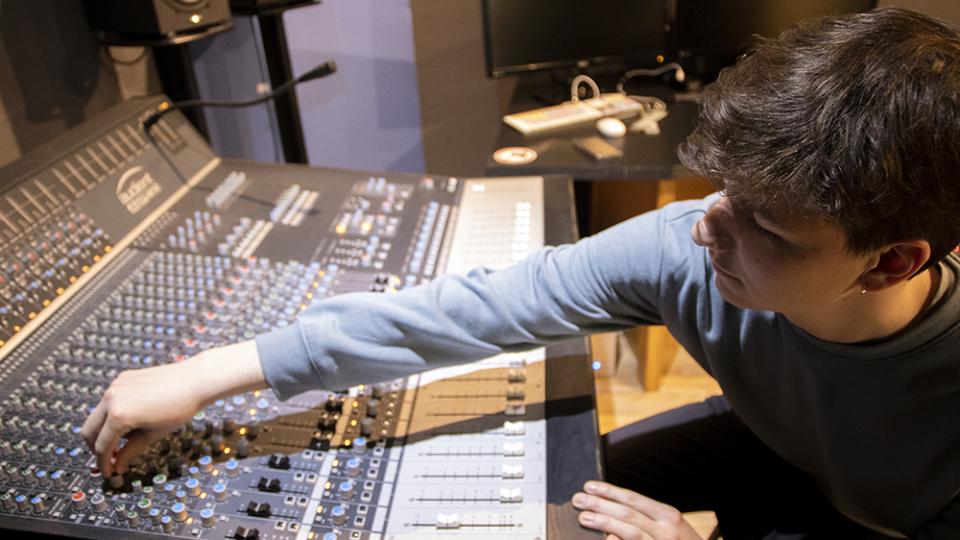 Student adjusts knobs on a mixing desk