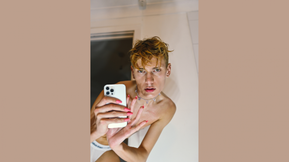 Subject taking a photo of himself in a mirror with wet hair and a silver necklace on.