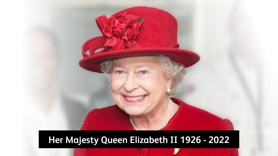 Her Majesty Queen Elizabeth II is wearing red attire and is smiling.