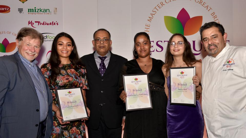 Olivia Parker-Smith, Prema Rebekah Kaur Sembi-Harding and Nekshia Alcee are holding winners certificates in formal dress, with two staff members, at the Zest Quest Asia Awards ceremony.