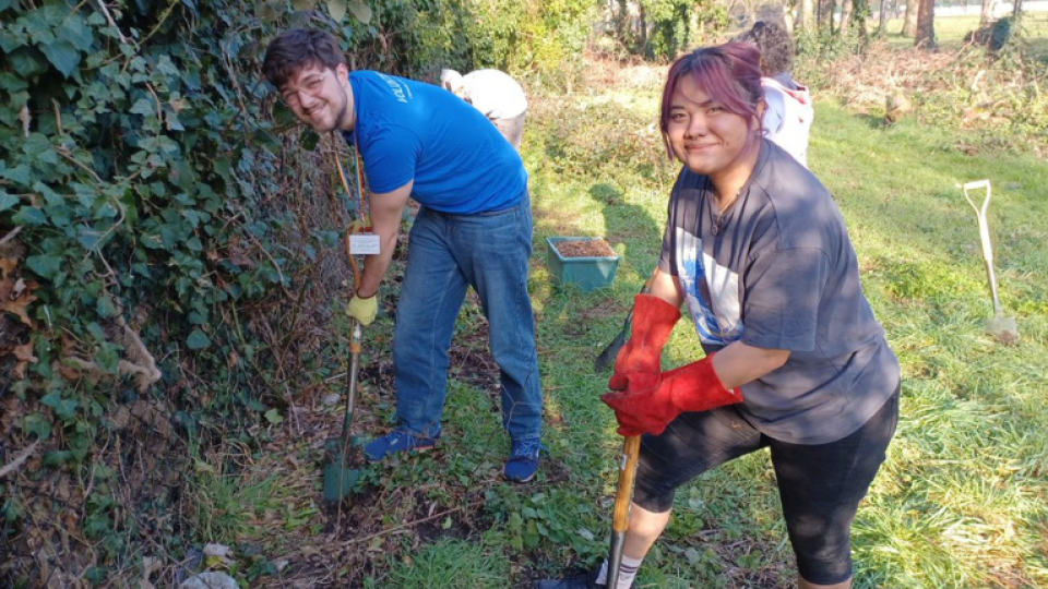 Two student volunteers digging grass as part of conservation work for volunteering week.