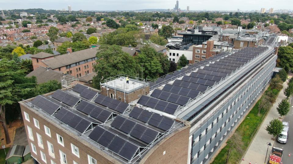 A view of solar panels on top of the University of West London's Ealing site, surrounded by buildings and greenery.