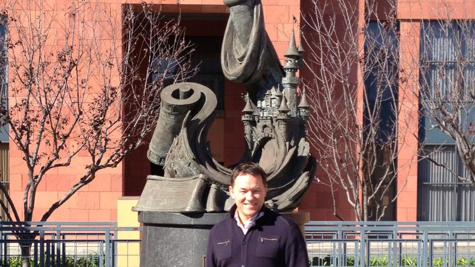 Peter Collyer is standing next to a sculpture of Mickey Mouse at Disneyland California.