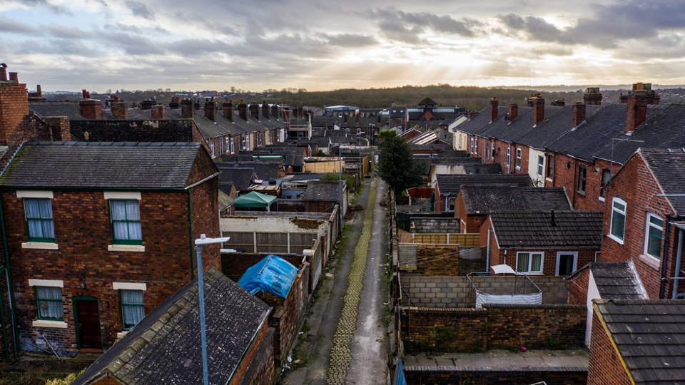 Rows of terraced houses with the sun peaking through clouds in the background.