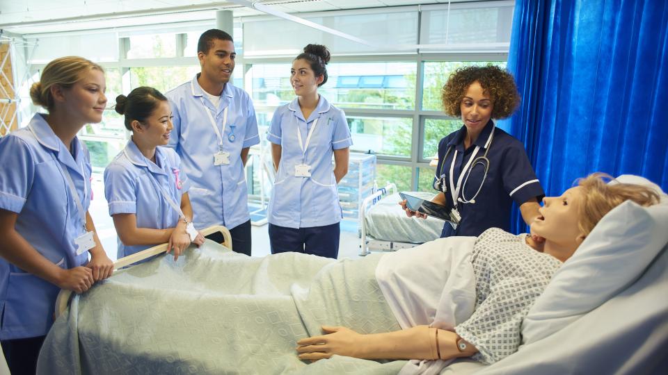 a class of student nurses gather around a bed