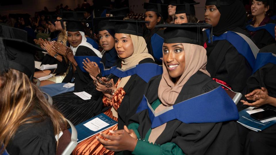 A group of graduands seated at the ceremony, clapping and looking towards the front.