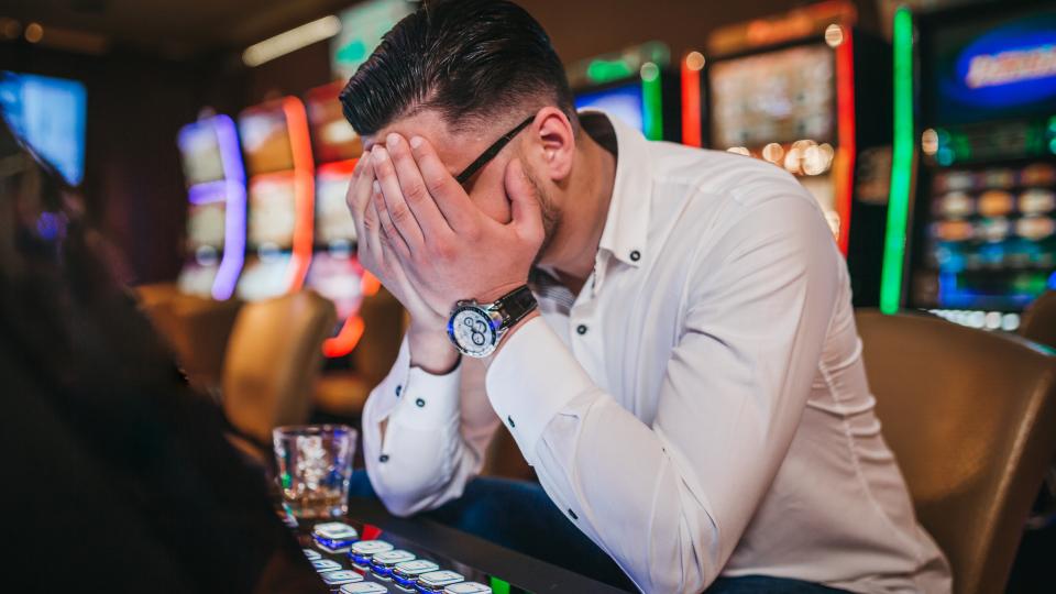 A man holds his head in his hands in front of a fruit machine
