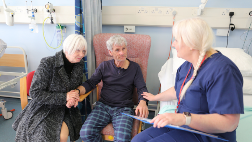 A patient with a family member seated whilst being reassured by a nursing staff member. 