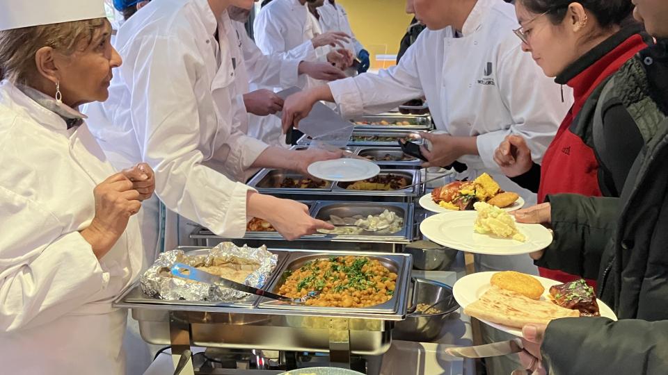 SCE staff, wearing chef whites, serve food to students