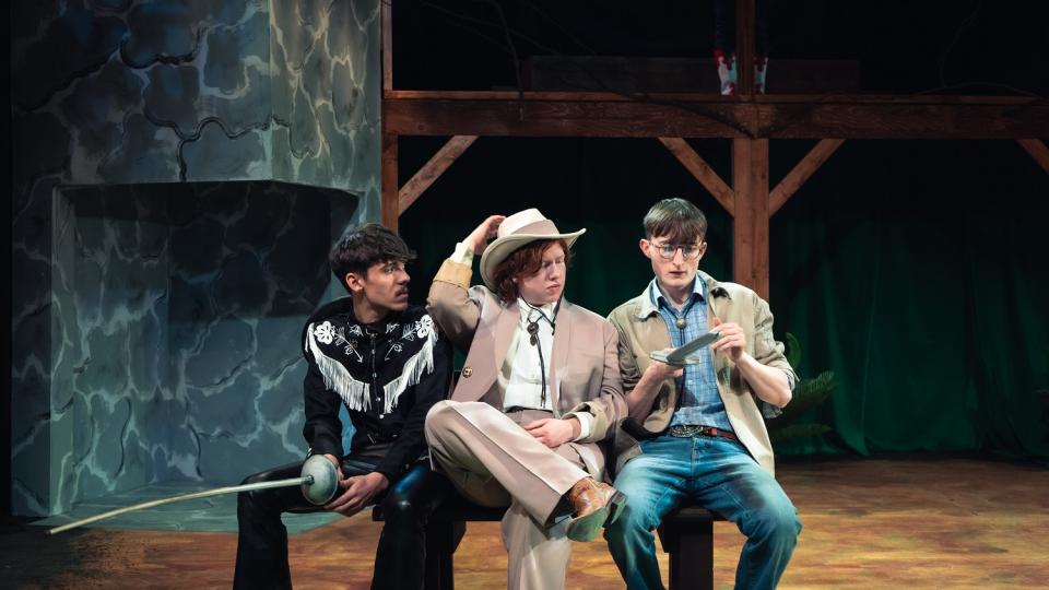 Three LCM students sat on a bench whlie performing in Twelfth Night. They are dressed like they are in a western.