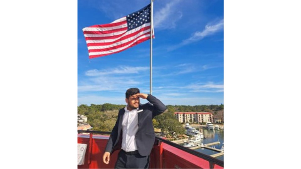 Rahul Dahiya is standing outside in front of a USA flag