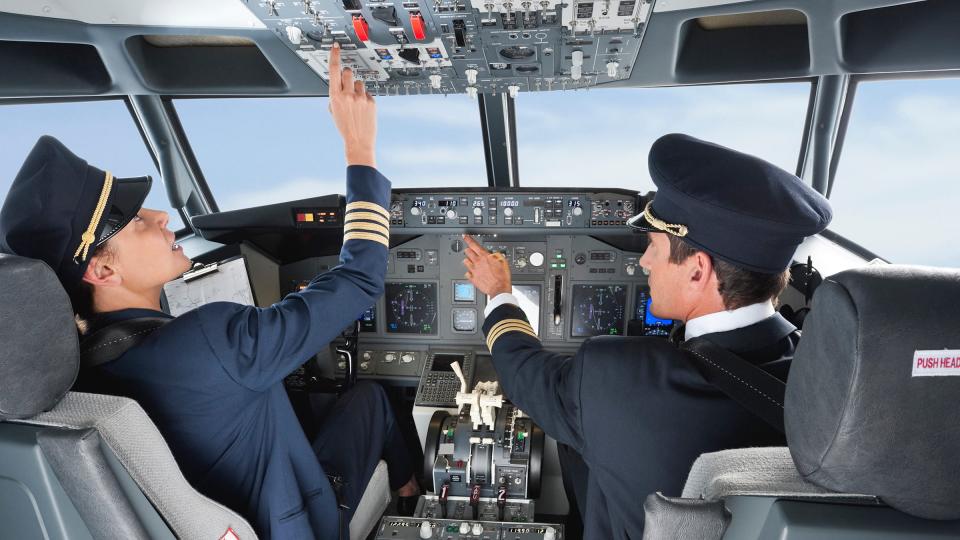 A female and male pilot in a cockpit pressing buttons
