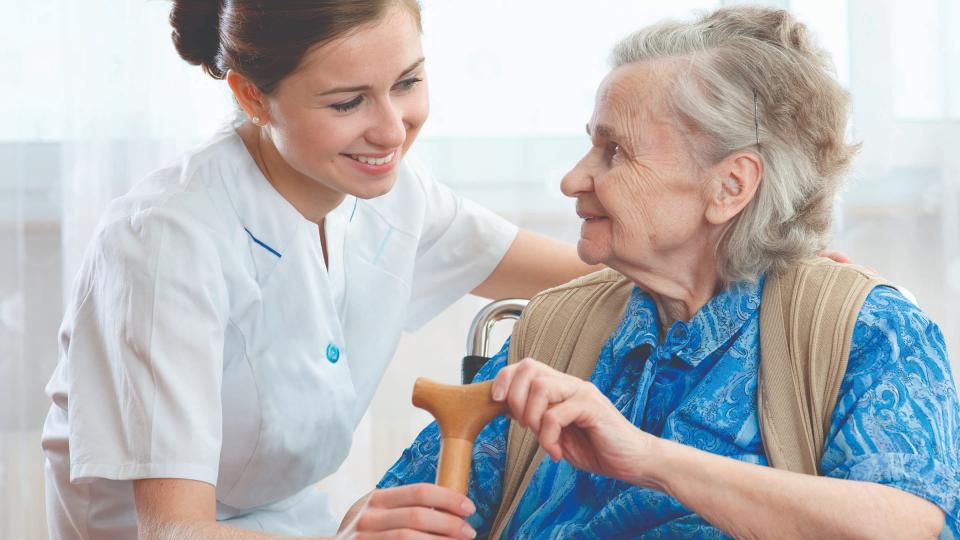 A smiling female nurse talking to a fan elderly woman with a walking stick