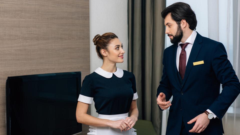A bearded man in a suit talking to a female cleaner