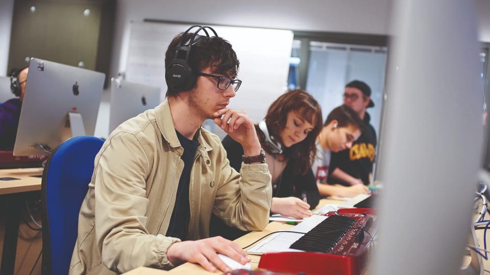 A male student wearing headphones and working on a keyboard and Mac