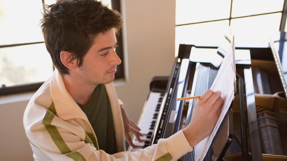 A male student making notes on sheet music whilst sitting at a piano