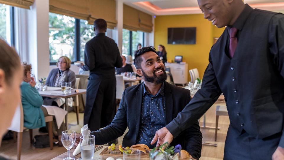 A male server pouring a drink for a gentleman in Pillars Restaurant